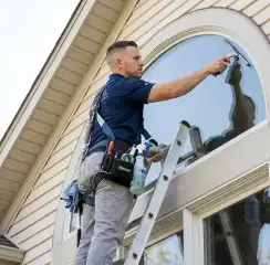 Professional window cleaner on a ladder using a squeegee to clean an exterior arched window, Pembroke Pines, FL.